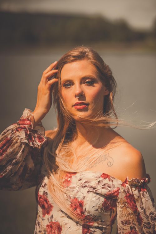 Free A serene portrait of a woman in a floral dress by a lake, exuding a warm and natural ambiance. Stock Photo