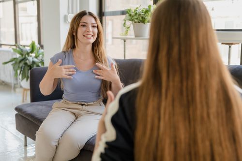 Free Two women chatting and using sign language indoors on a sofa. Stock Photo