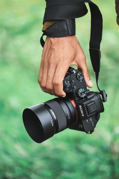 Close-up of a hand holding a camera against a green outdoor backdrop, capturing the essence of photography.