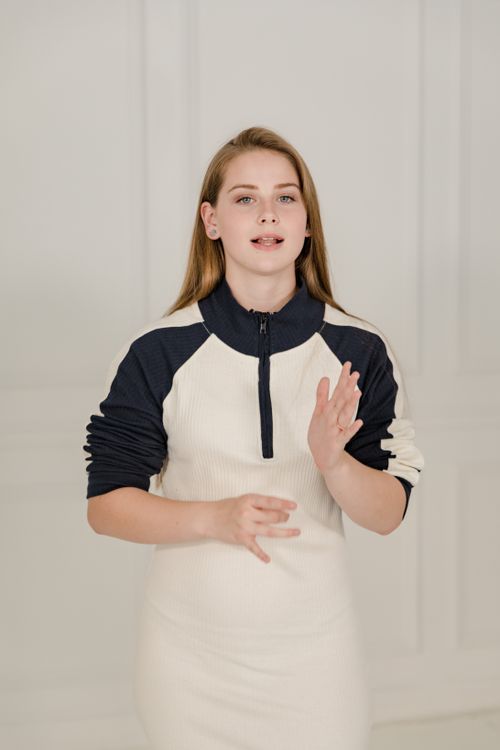Free Portrait of a young woman with blond hair gesturing indoors, wearing a stylish dress. Stock Photo