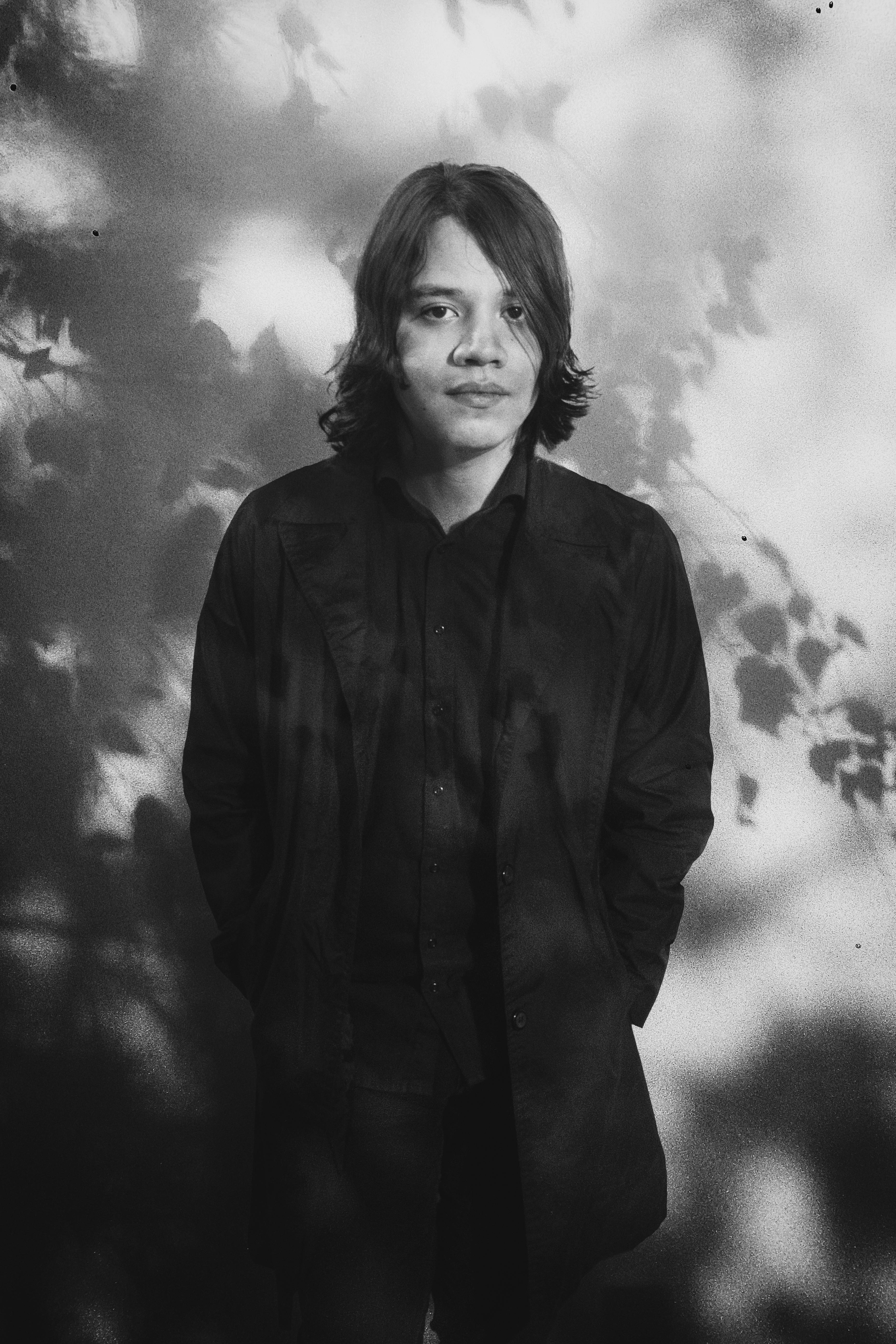 Artistic grayscale portrait of a man in a black coat with shadow patterns.