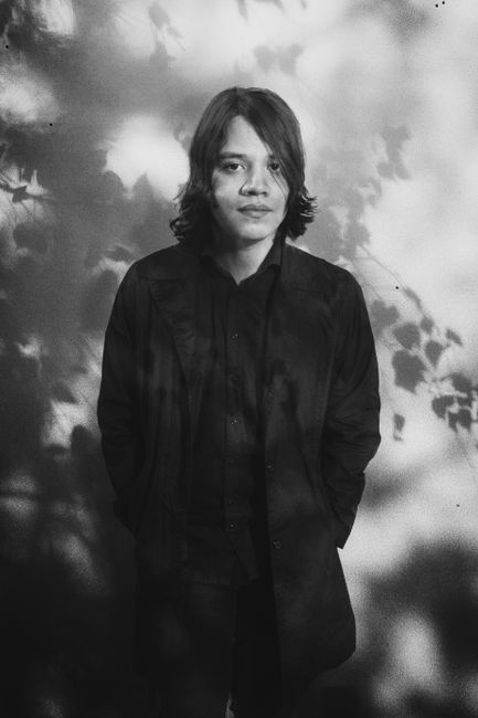 Artistic grayscale portrait of a man in a black coat with shadow patterns.