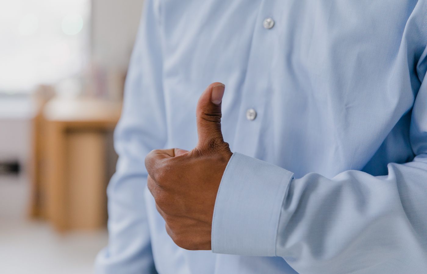 Close-up of businessman giving a thumbs up, wearing a light blue shirt indoors.
