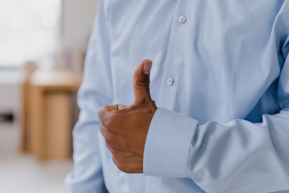 Close-up of businessman giving a thumbs up, wearing a light blue shirt indoors.