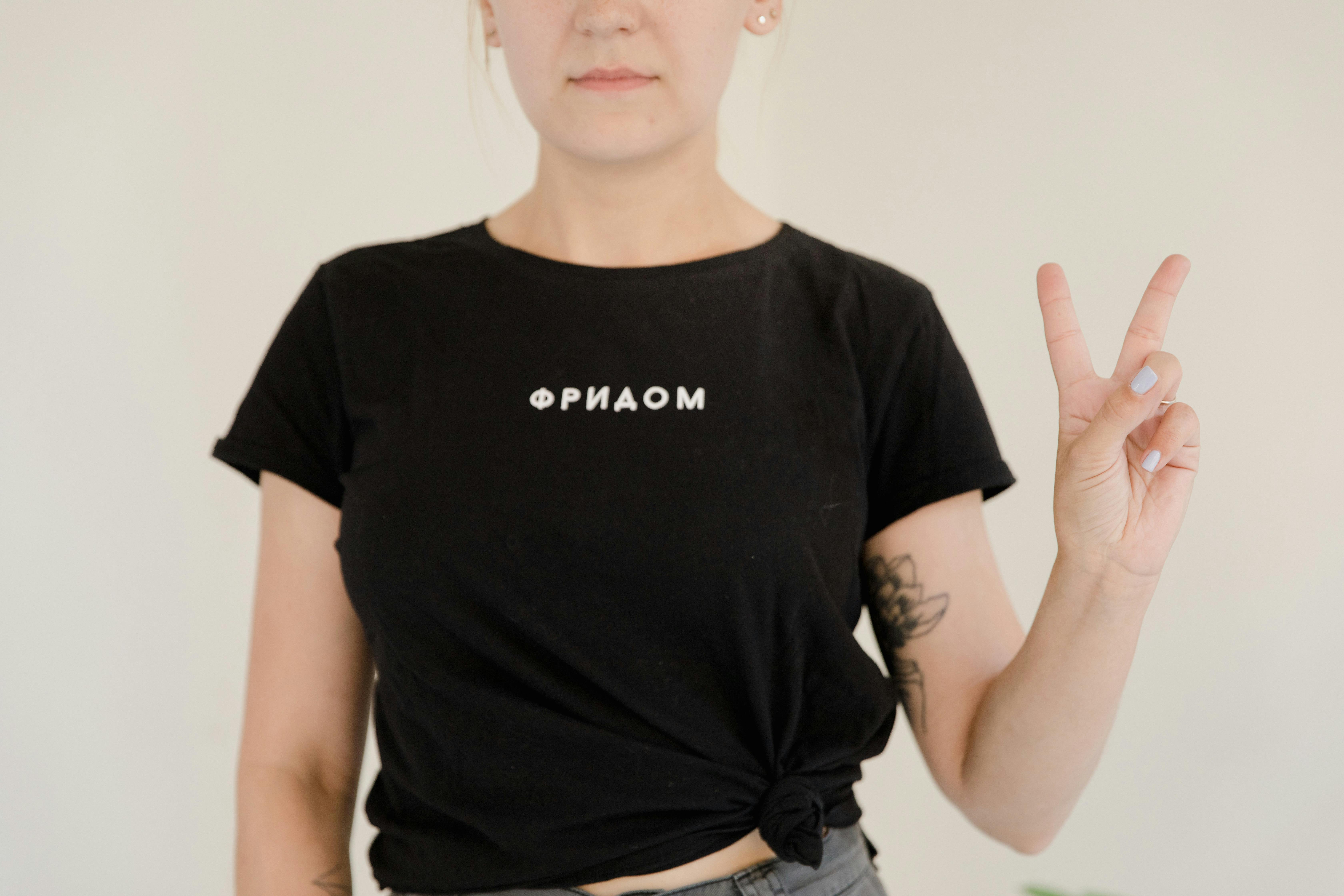 Close-up of a woman wearing a black t-shirt with a peace sign gesture, symbolizing freedom and style.