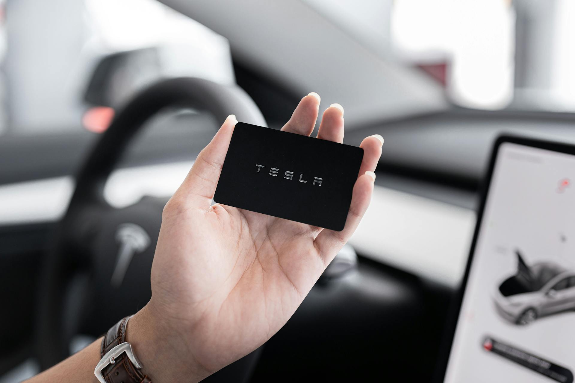 Close-up of a hand holding a key card inside a modern car interior with digital display.