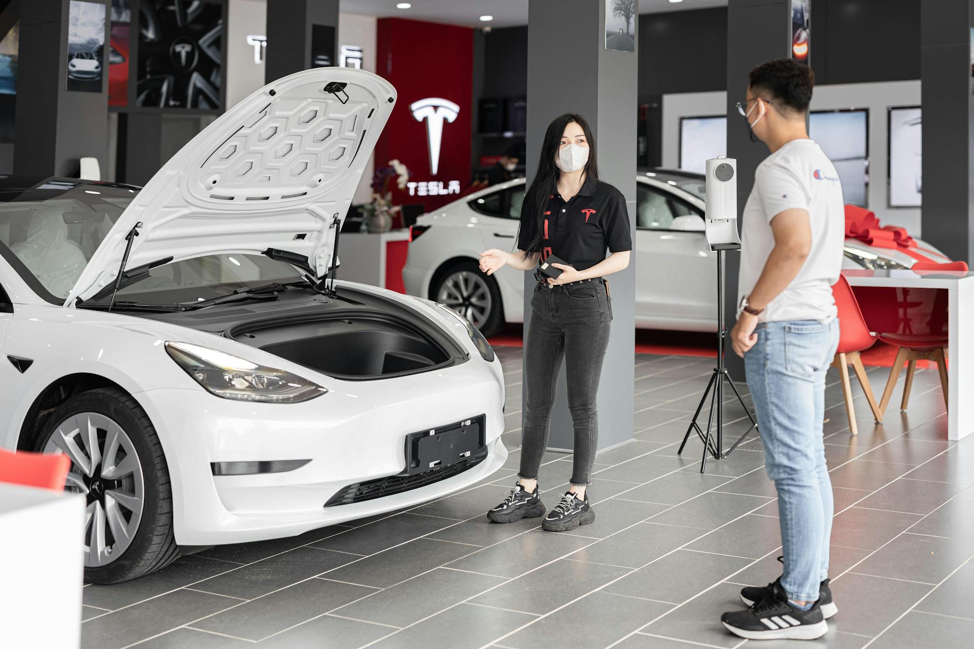 A customer talks with a sales representative about a Tesla Model 3 in a car dealership, showcasing the electric car's features.