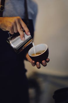 Barista skillfully pours milk into a coffee cup creating fresh froth.