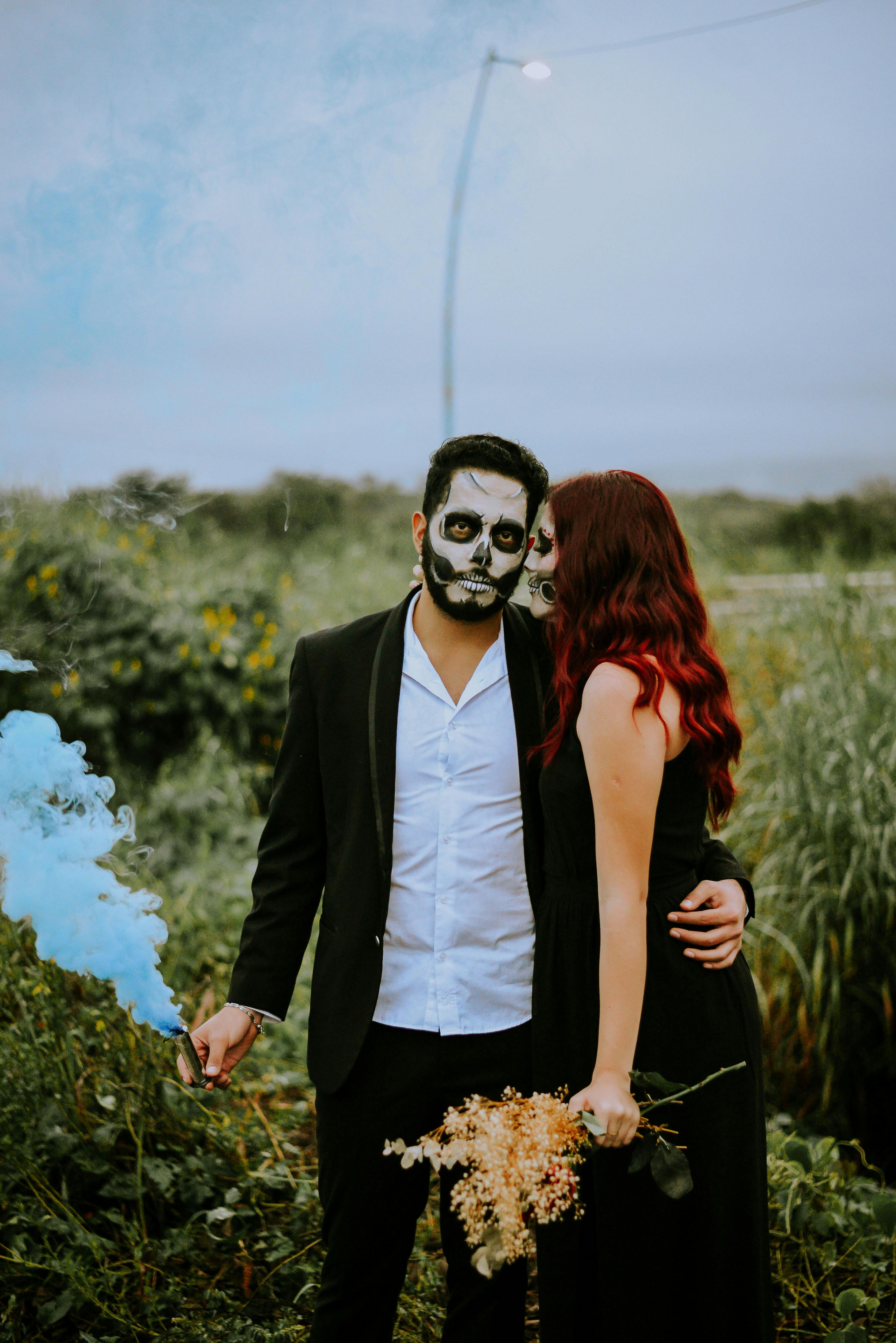 Couple celebrating Dia de los Muertos with face paint and traditional costumes outdoors.