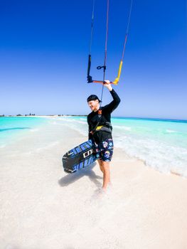 Man enjoying kiteboarding on a tropical beach with clear blue sea and sky.
