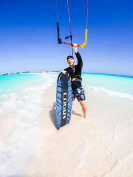 Man enjoying kiteboarding on a sunny beach with clear turquoise water and vibrant sky.