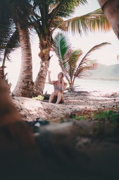 Woman enjoying a sunny day under palm trees on a sandy beach, capturing tropical vibes.