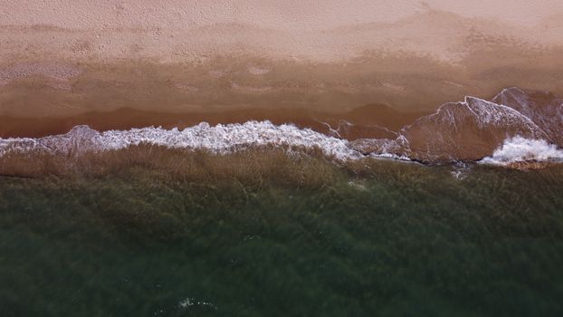 Drone shot of waves hitting a sandy beach in Latina, Lazio, Italy.