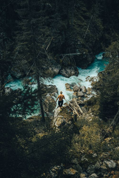 Free A topless hiker views a stunning mountain river, surrounded by lush forest. Stock Photo