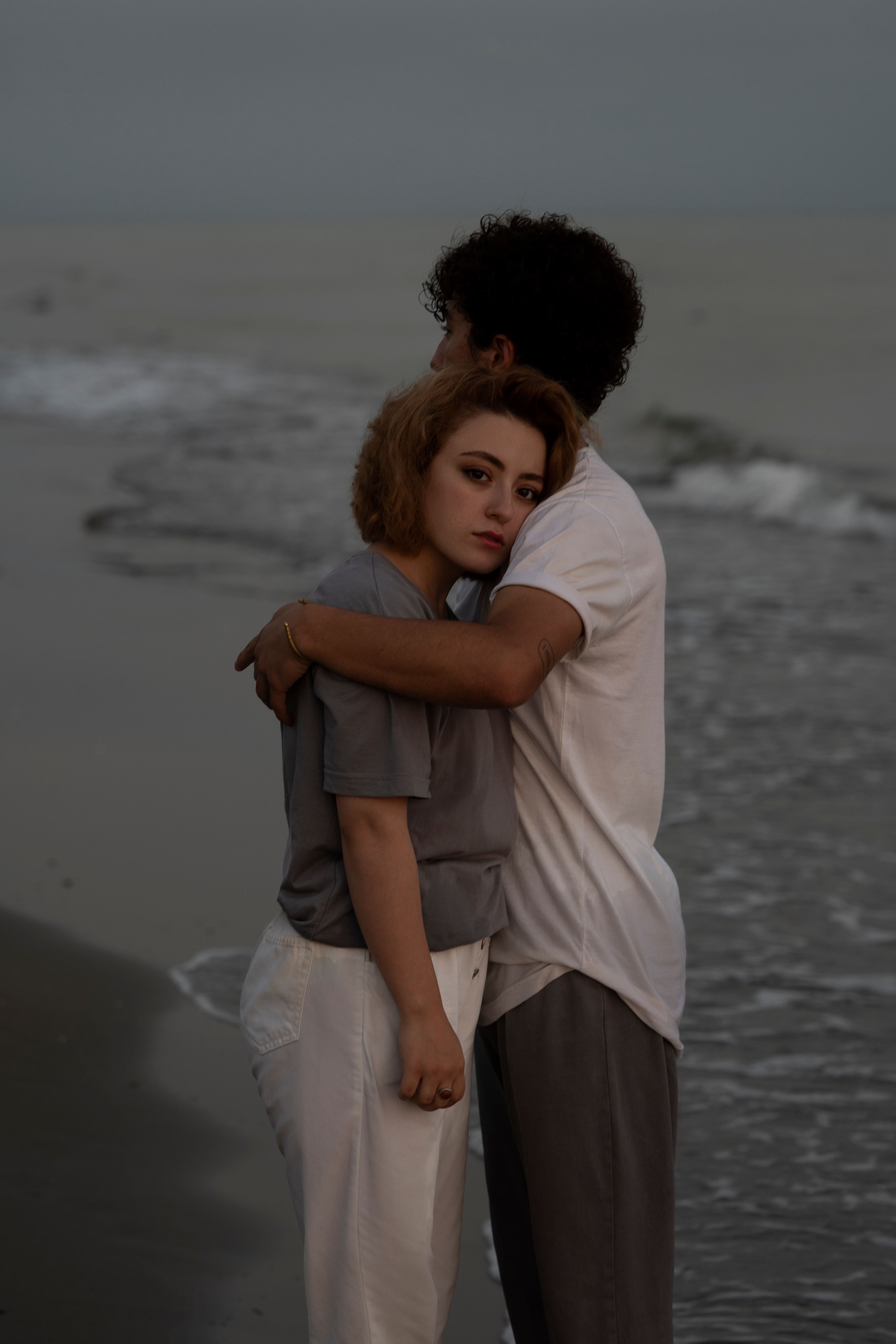 A romantic moment captured as a couple embraces on a serene beach with waves in the background.