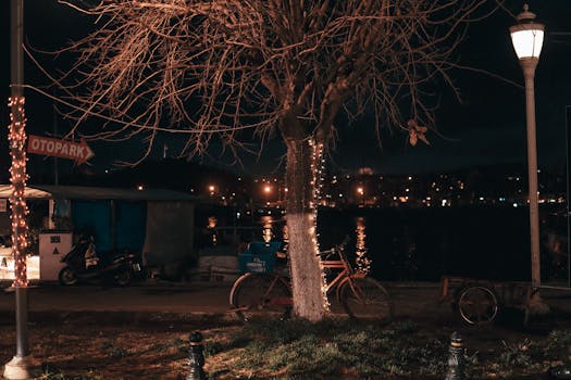 A serene urban night scene with a bicycle by a river, city lights reflecting on the water.