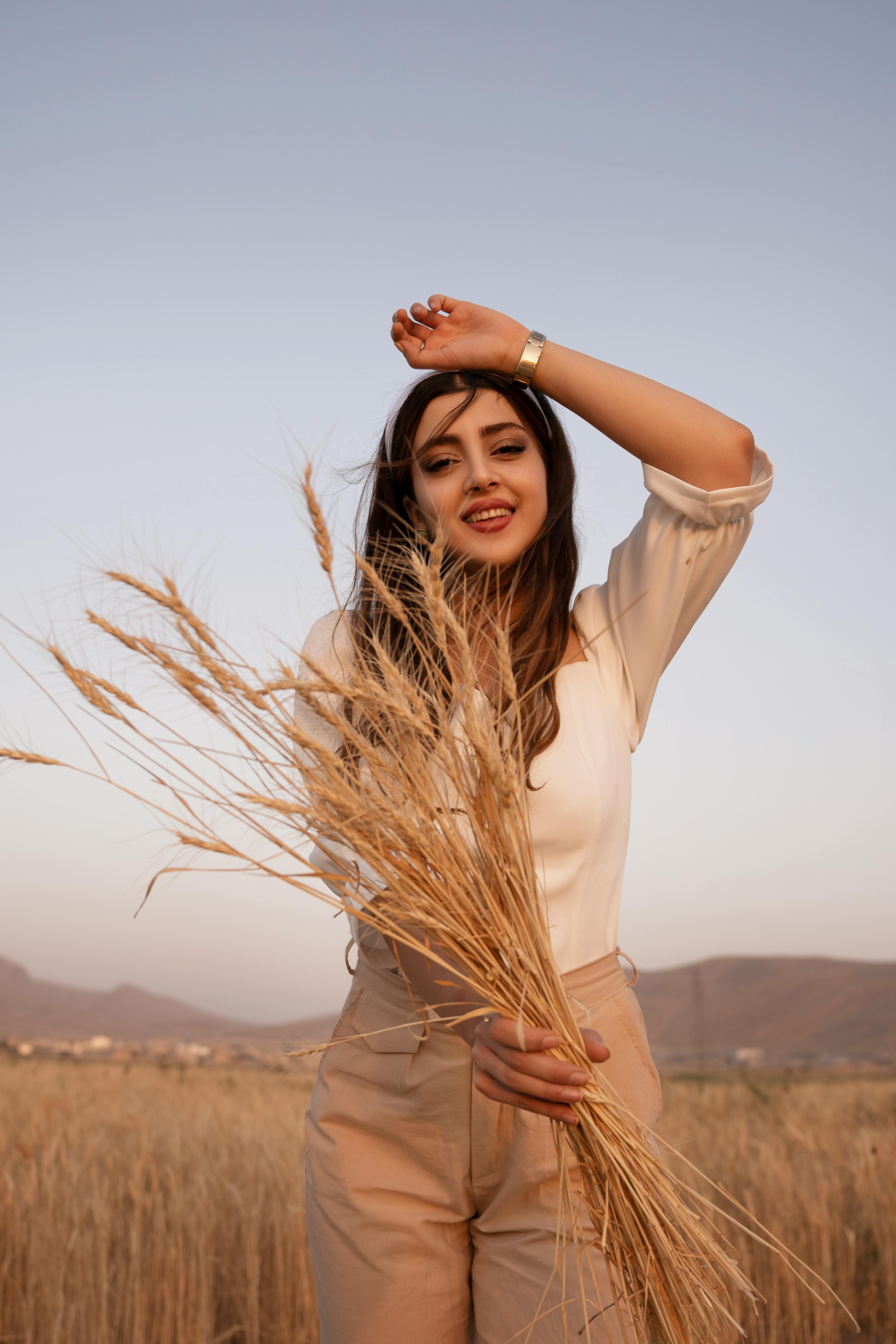 A young woman joyfully holding dried wheat stalks in a sunlit field.