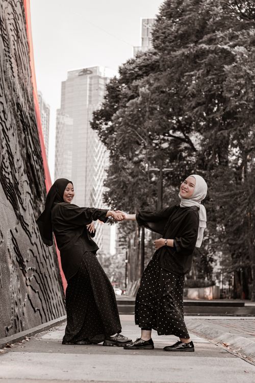 Free Two women in hijabs happily holding hands in an outdoor urban setting. Stock Photo