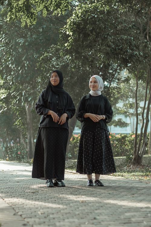 Free Two women in hijabs walk on a sunlit pathway surrounded by trees, enjoying a serene moment. Stock Photo