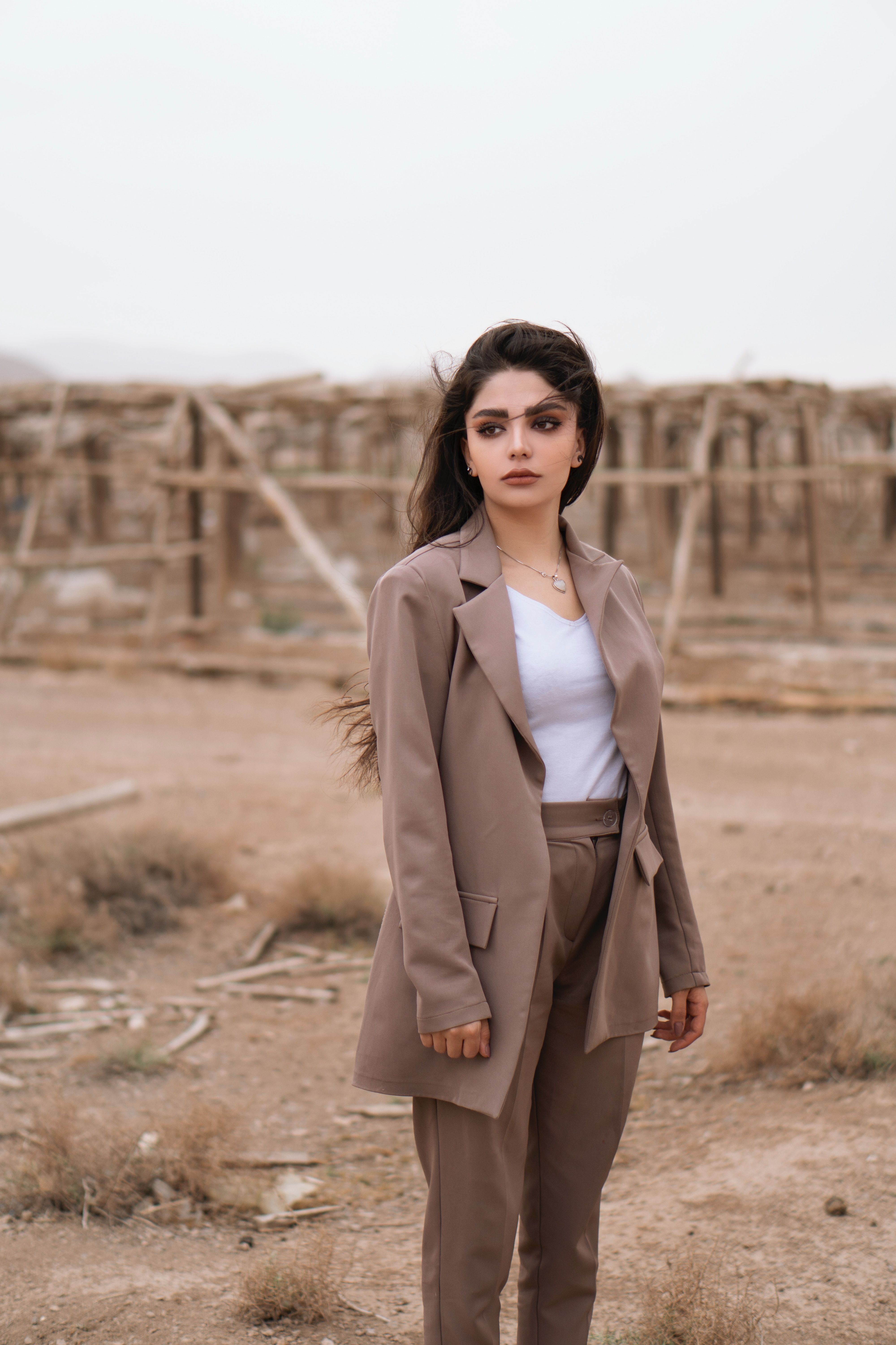 Woman in a neutral suit poses confidently in a rustic outdoor setting.