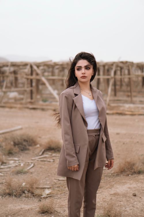 Free Woman in a neutral suit poses confidently in a rustic outdoor setting. Stock Photo