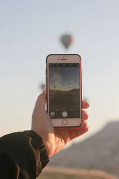 A person photographs hot air balloons with a smartphone, perfect for travel themes.
