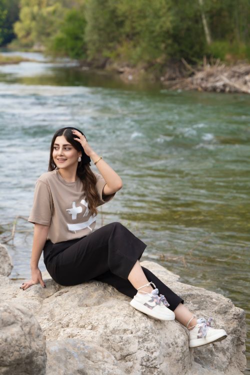 Free Woman sitting on rocks by a peaceful river, enjoying a serene outdoor moment. Stock Photo