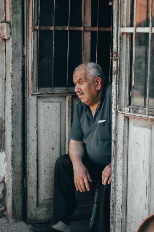 Free Senior man seated in rustic doorway, reflecting a moment of relaxation and contemplation. Stock Photo