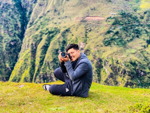 Man Sitting on Grass While Taking Photo with a Camera