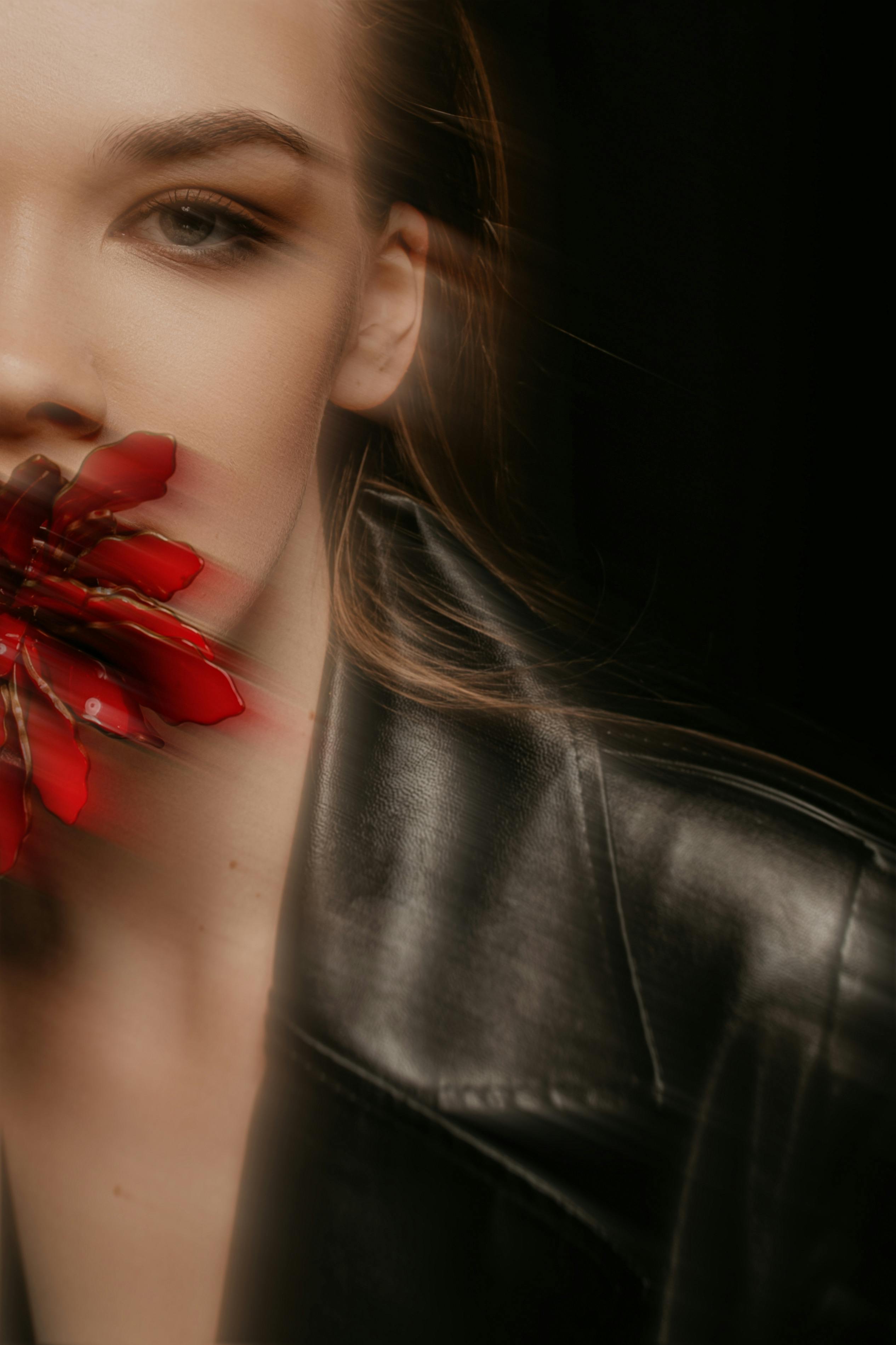 Creative portrait featuring a woman with a red flower on her face, symbolizing beauty and mystery.