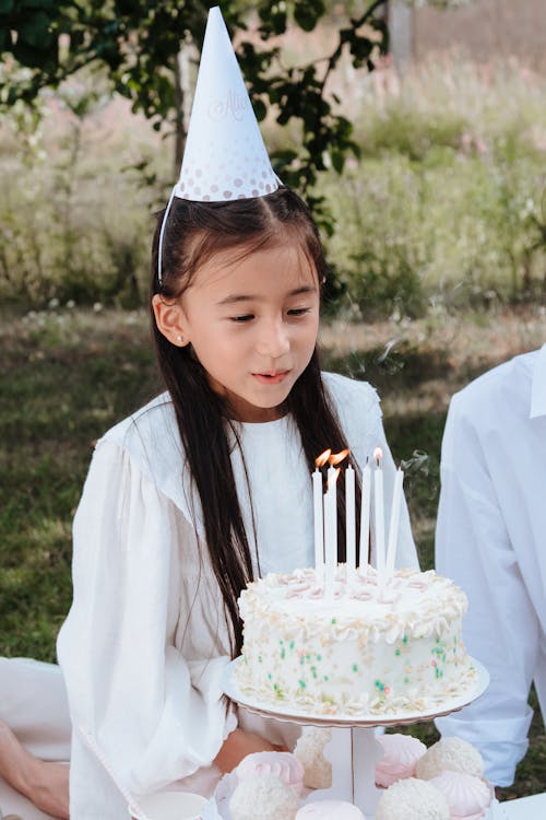 Girl in Party Hat Blowing Candles on Birthday Cake