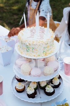 Three-tier dessert stand at an outdoor birthday party featuring a decorated cake and cupcakes.