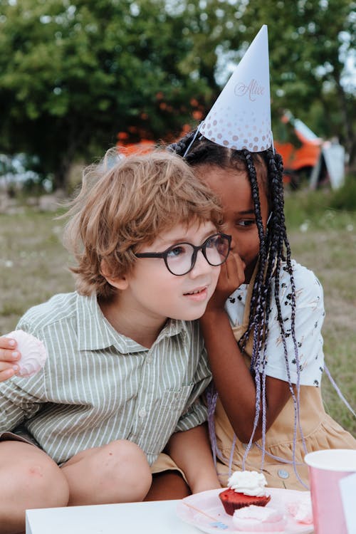 Free Girl Whispering to Boys Ear at Birthday Party in Garden Stock Photo
