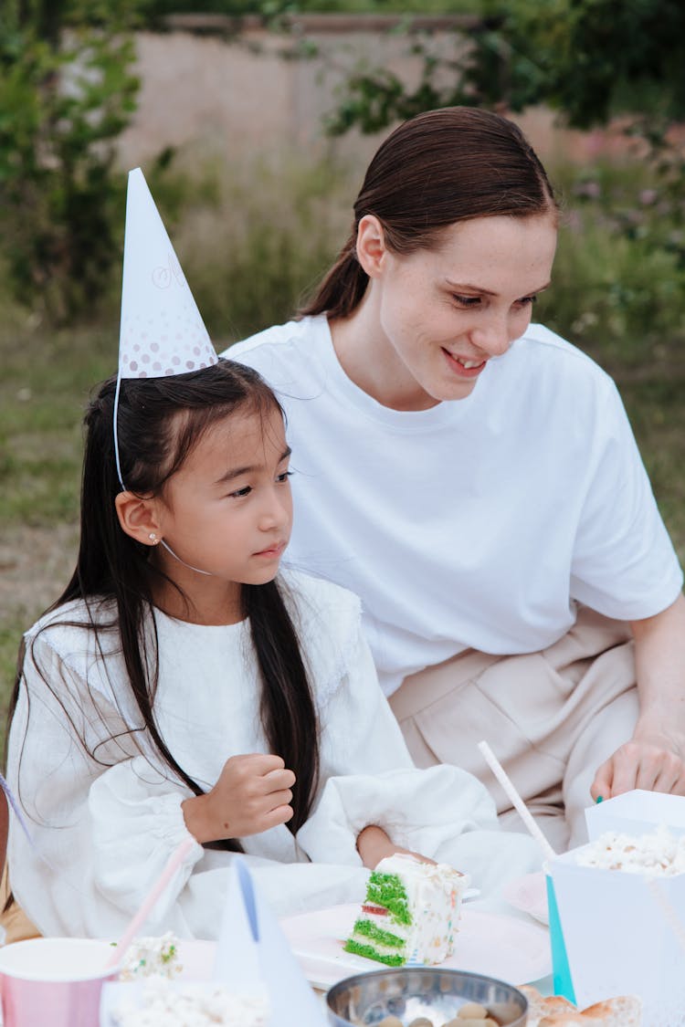 Smiling Woman And Girl In Party Hat At Table In Garden