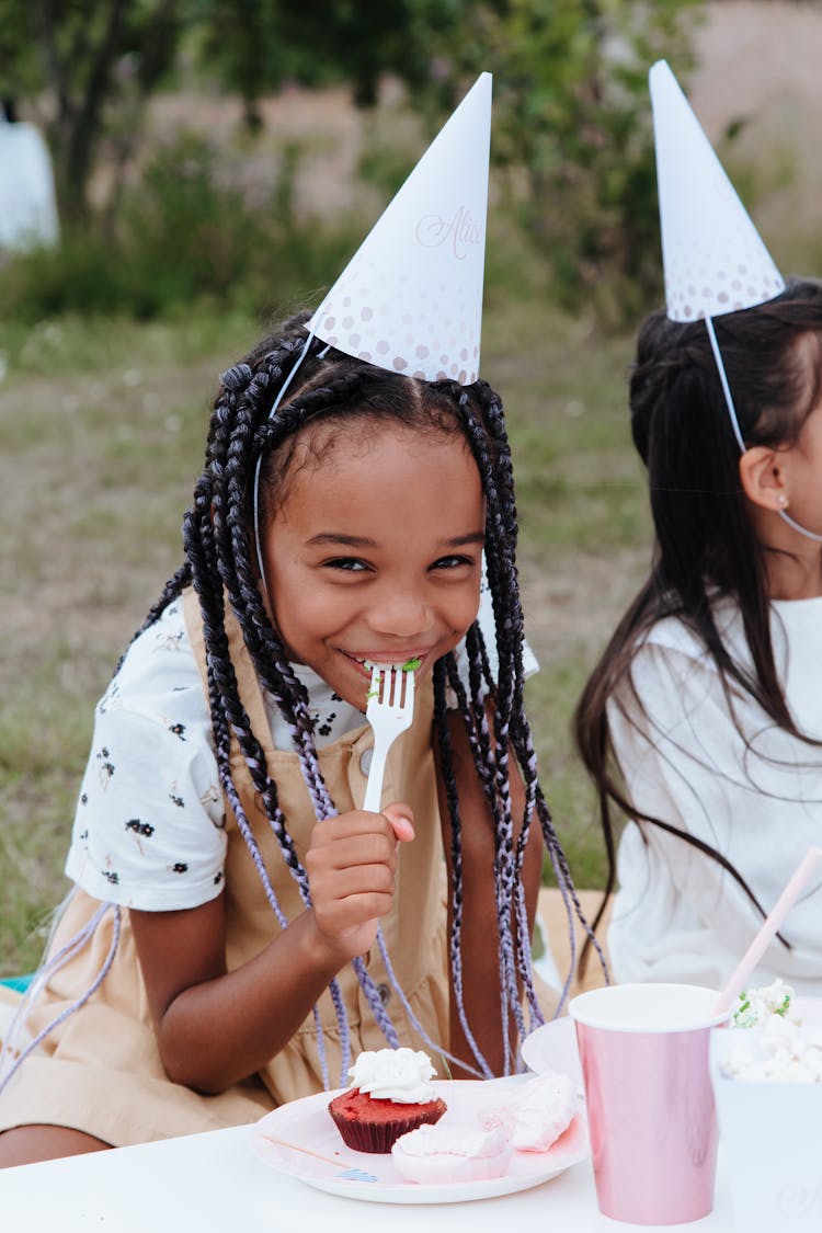 Smiling Girl In Party Hat Eating Cupcake At Garden Party