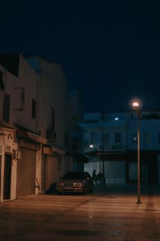 A quiet, dimly lit alley at night featuring urban buildings and a lone street lamp casting moody shadows.