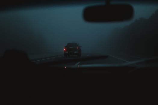 A car driving through a foggy road at night, creating a moody atmosphere.