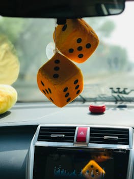 Fuzzy dice hanging from a car's rearview mirror with blurred road view.