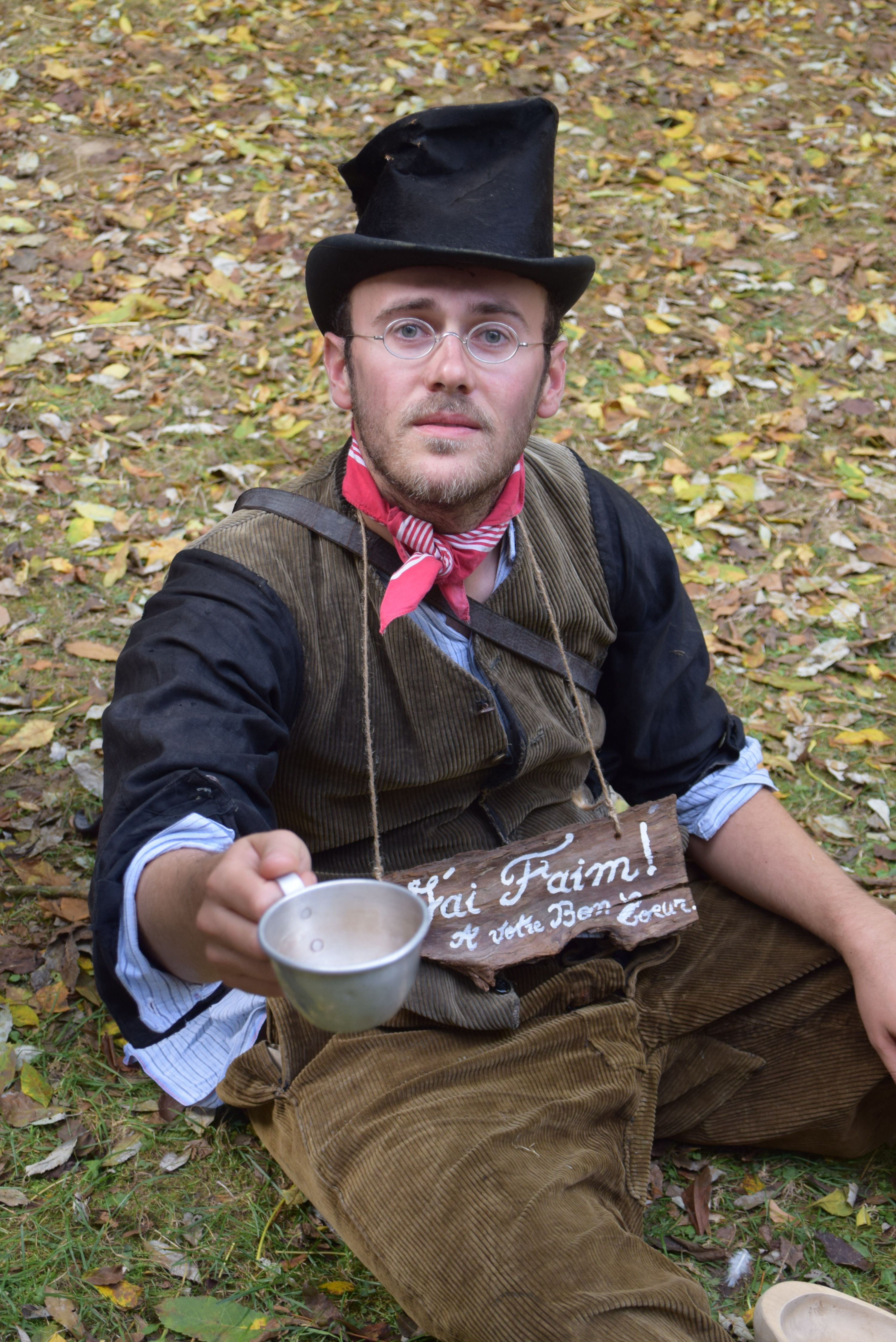 Portrait of a man in vintage costume holding a cup, sitting on autumn leaves.