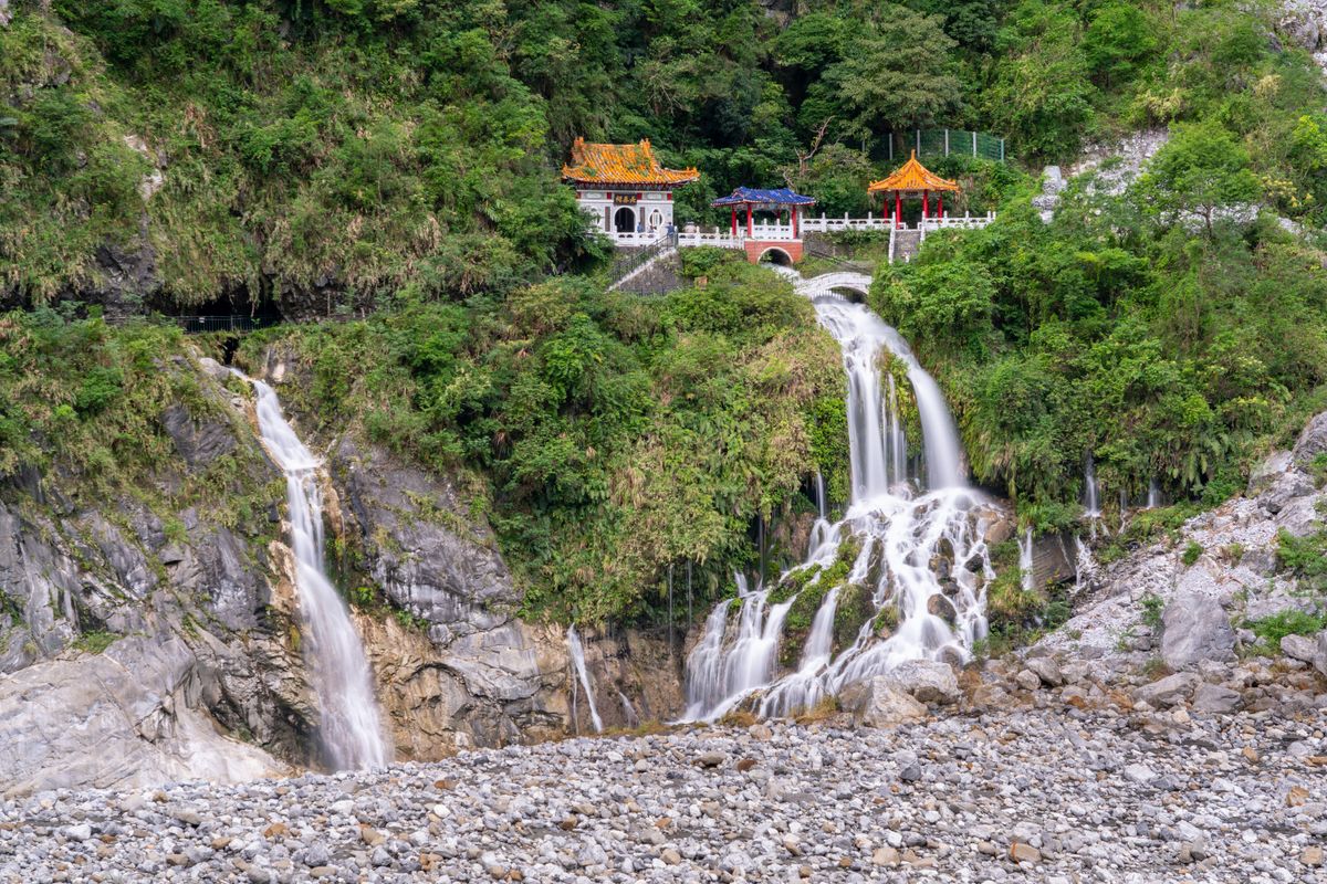 The Eternal Spring Shrine, a small temple with orange roofs perched above twin waterfalls spilling down a rocky slope into scree