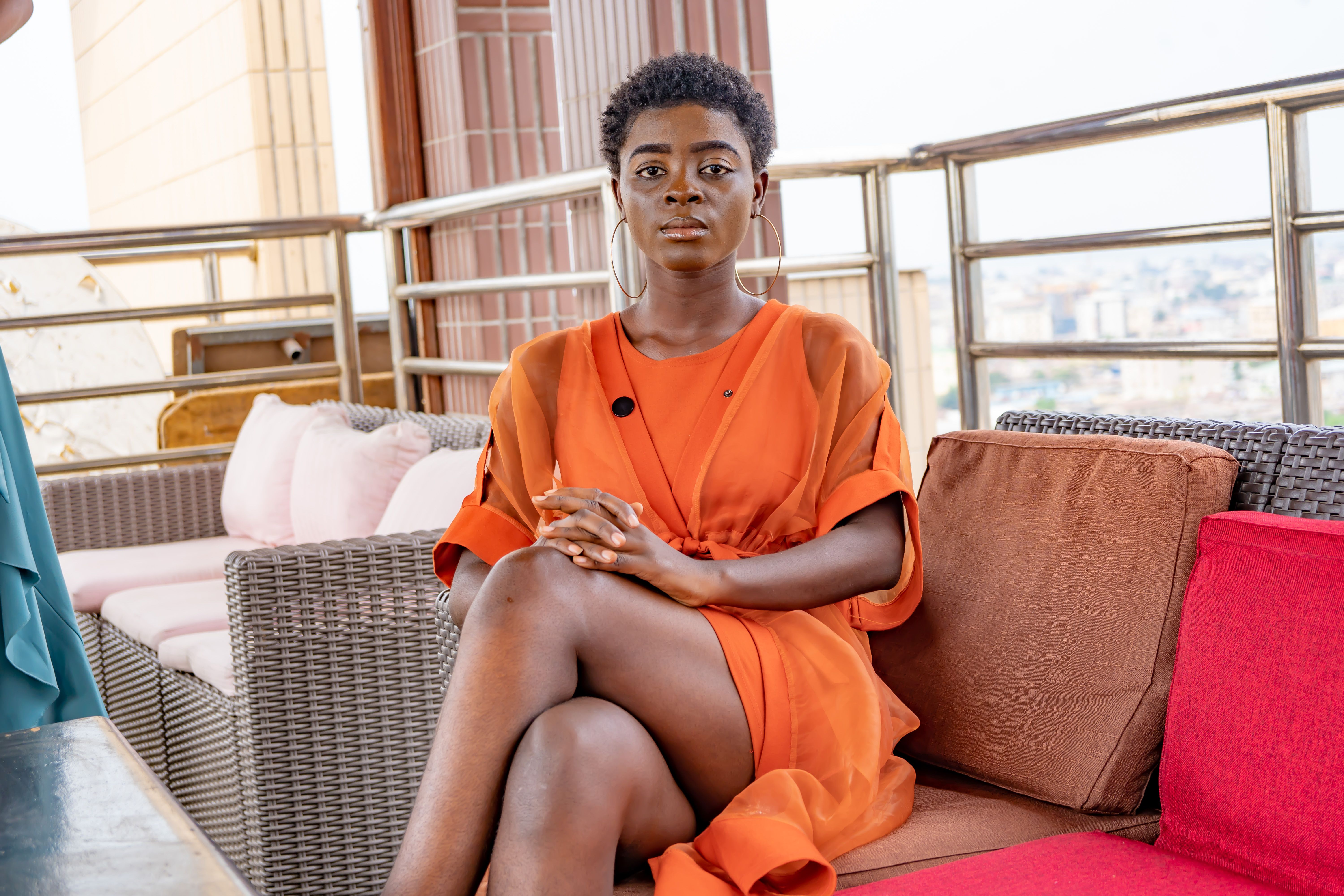Woman in her orange dress sitting on sofa, Congo