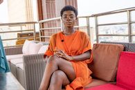 Elegant woman in an orange dress seated on a rooftop lounge in Brazzaville, conveying modern style and confidence.