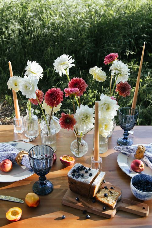 Free Elegant outdoor table setting with flowers, cake, and fruit for a delightful gathering. Stock Photo