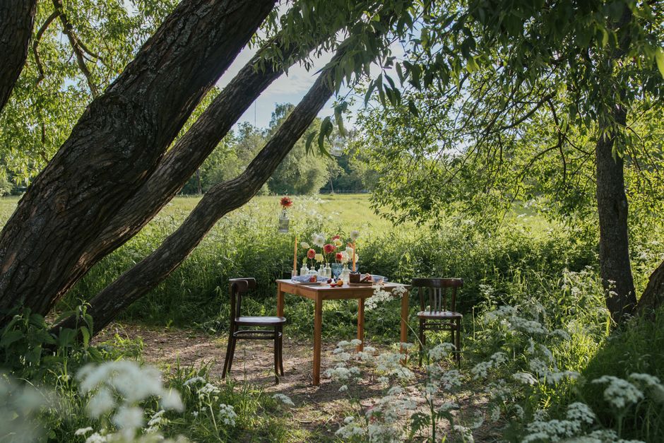 A serene outdoor dining setup with flowers and trees in a lush countryside location.