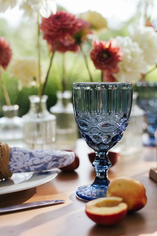 Free Chic outdoor table scene with blue glass surrounded by flowers and fruit. Stock Photo