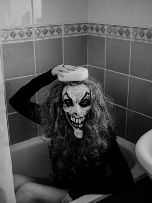 Woman Wearing Spooky Mask Sitting in Bathtub 