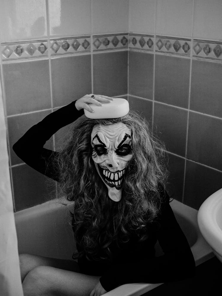 Woman Wearing Spooky Mask Sitting In Bathtub 