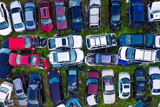 High-angle shot of various damaged cars in a junkyard surrounded by greenery.