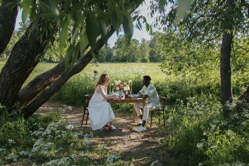 Free A couple enjoying a romantic picnic in a serene outdoor setting surrounded by lush greenery. Stock Photo