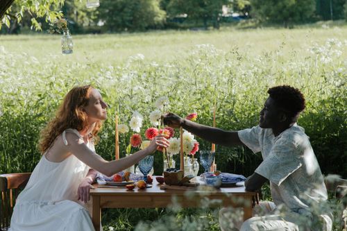 Free Interracial couple enjoying a romantic picnic surrounded by lush greenery in a farm field. Stock Photo